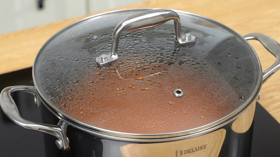 Close-up of condensation on a vented glass lid covering a DELUXE pot with two metal side handles.
